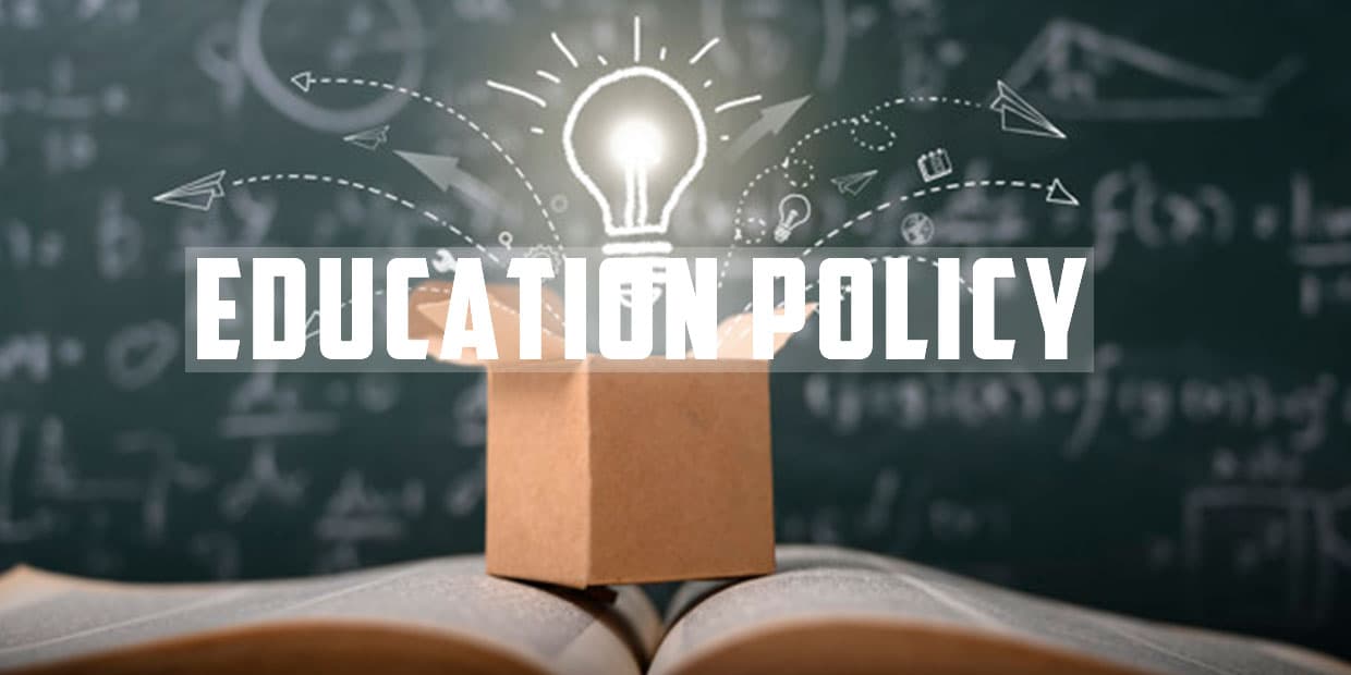 Education Policy concept with glowing light bulb emerging from a box placed on an open book, with chalkboard equations and icons in the background